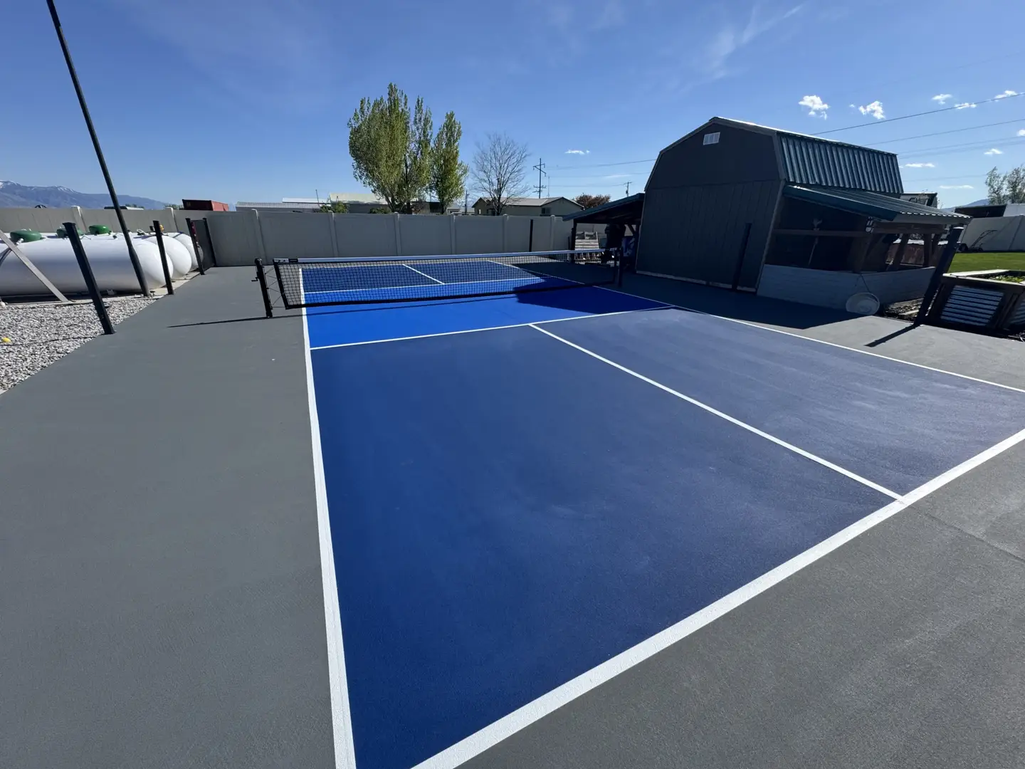 Vibrant blue pickleball court with grey surround and a barn-style building.