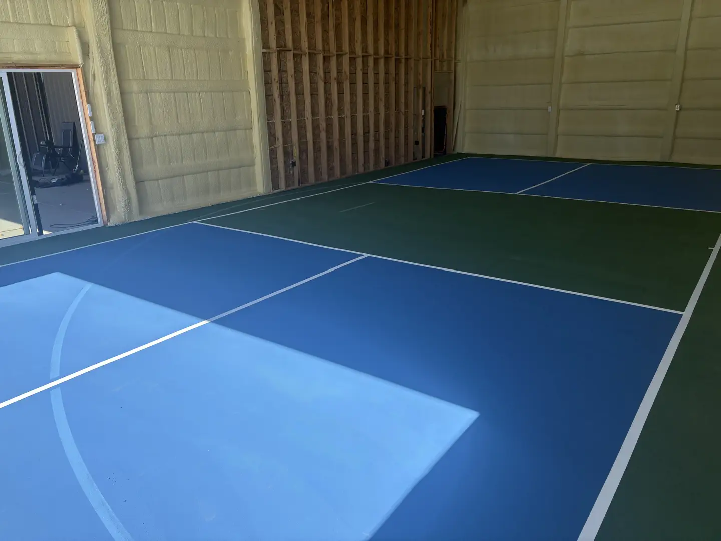 Newly painted indoor pickleball court with blue and green surfaces.