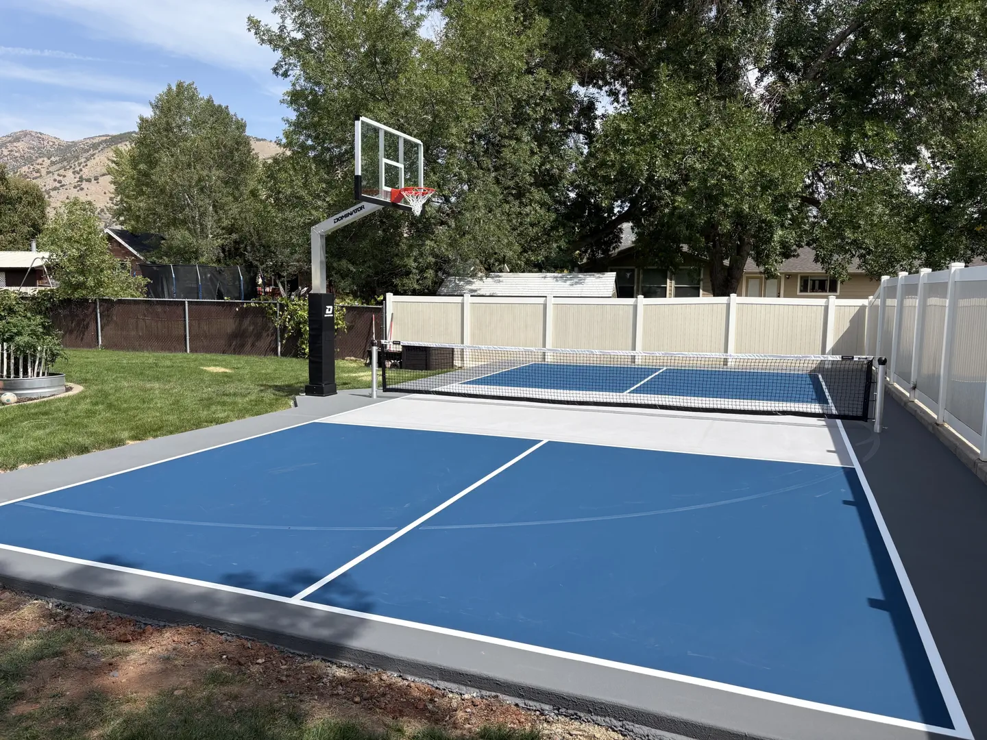 Blue pickleball court with basketball hoop in backyard