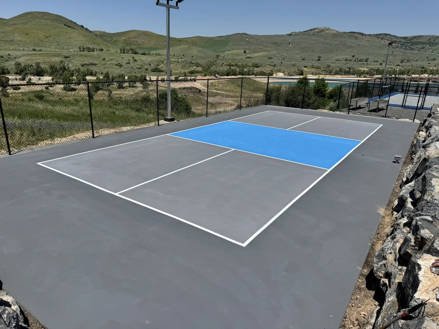 Newly painted pickleball court with blue and gray surface, surrounded by hills.