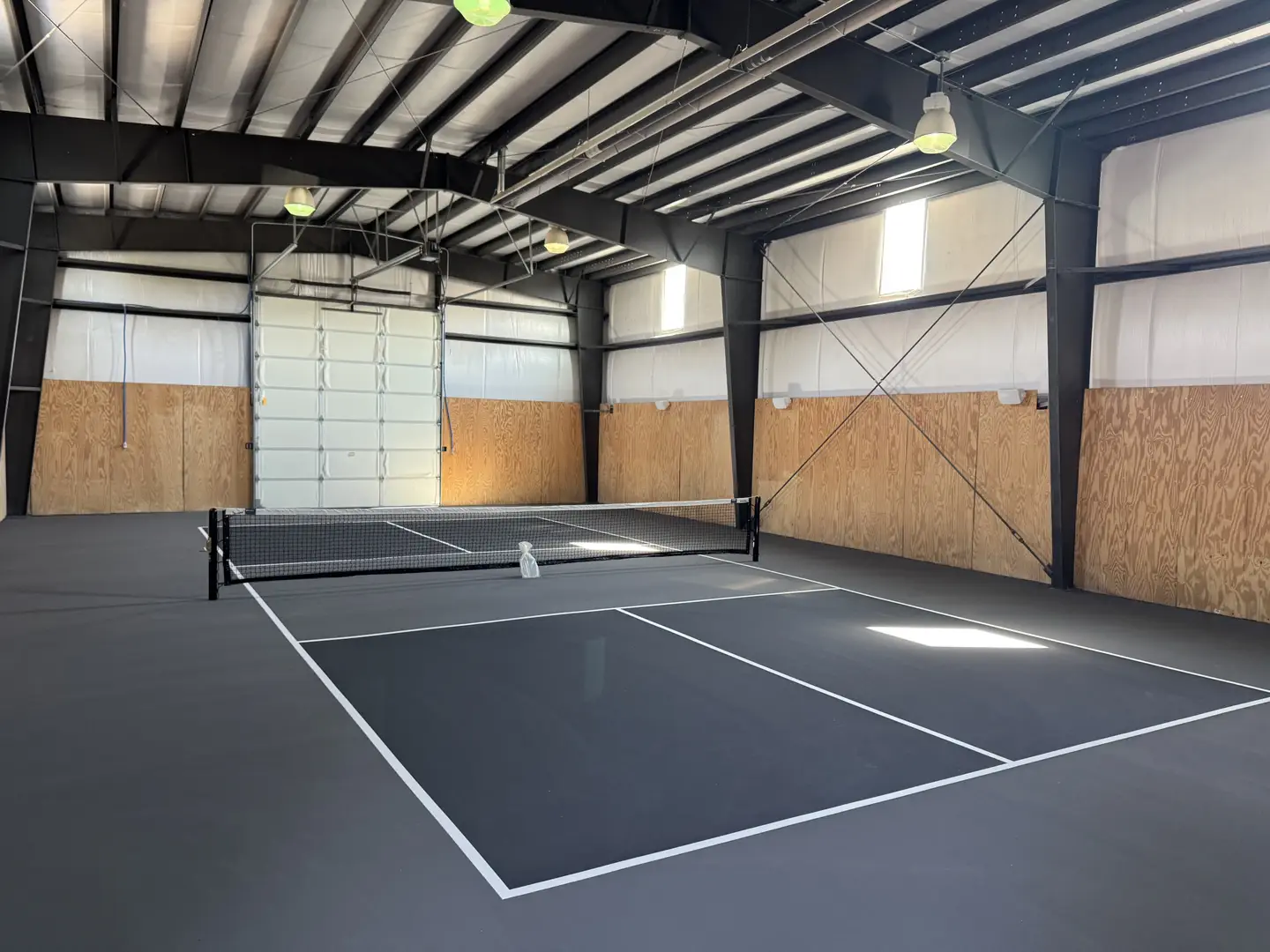 Indoor pickleball court with dark grey surface and white lines.