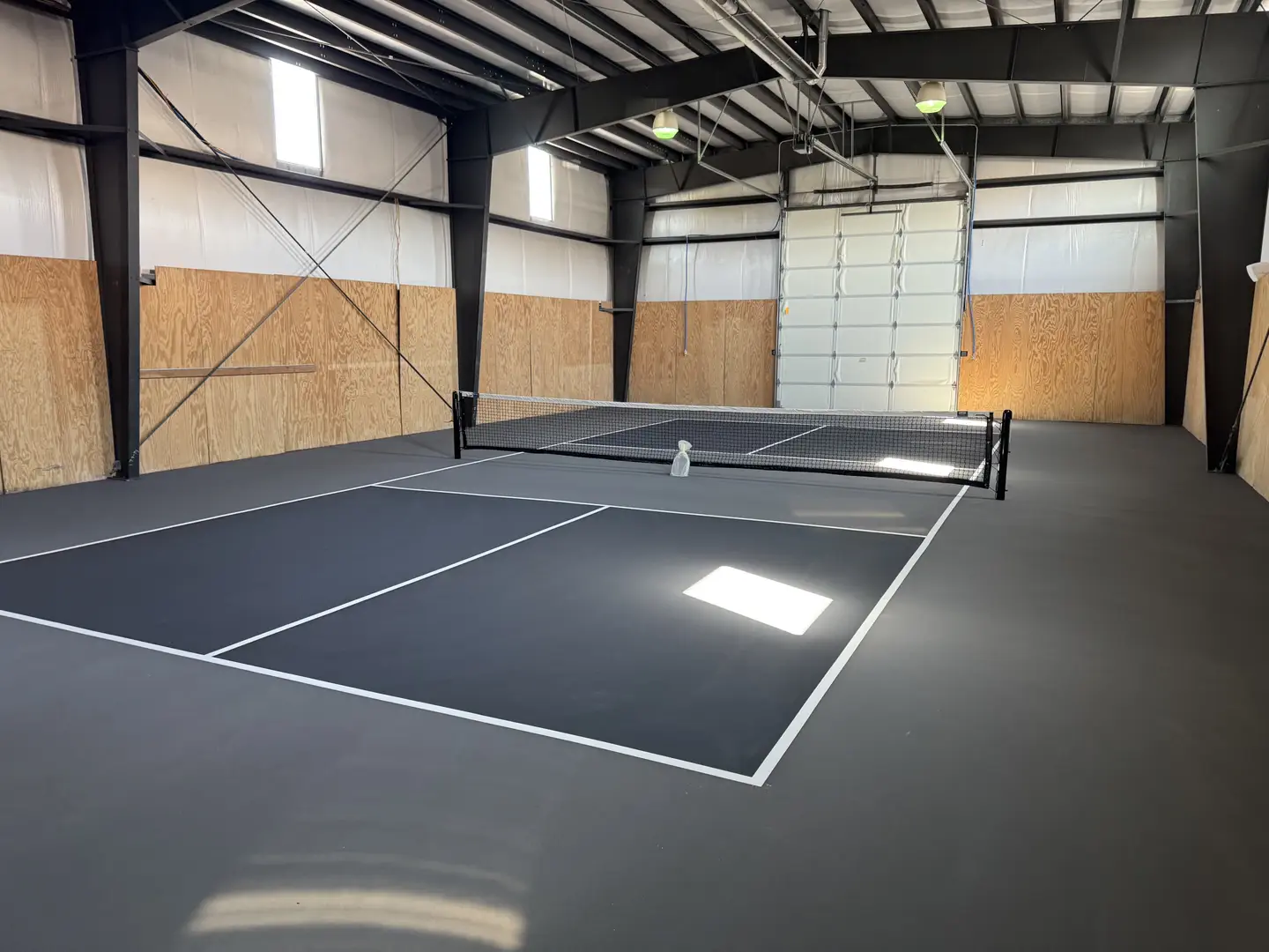 Indoor pickleball court with dark grey surface and white lines.