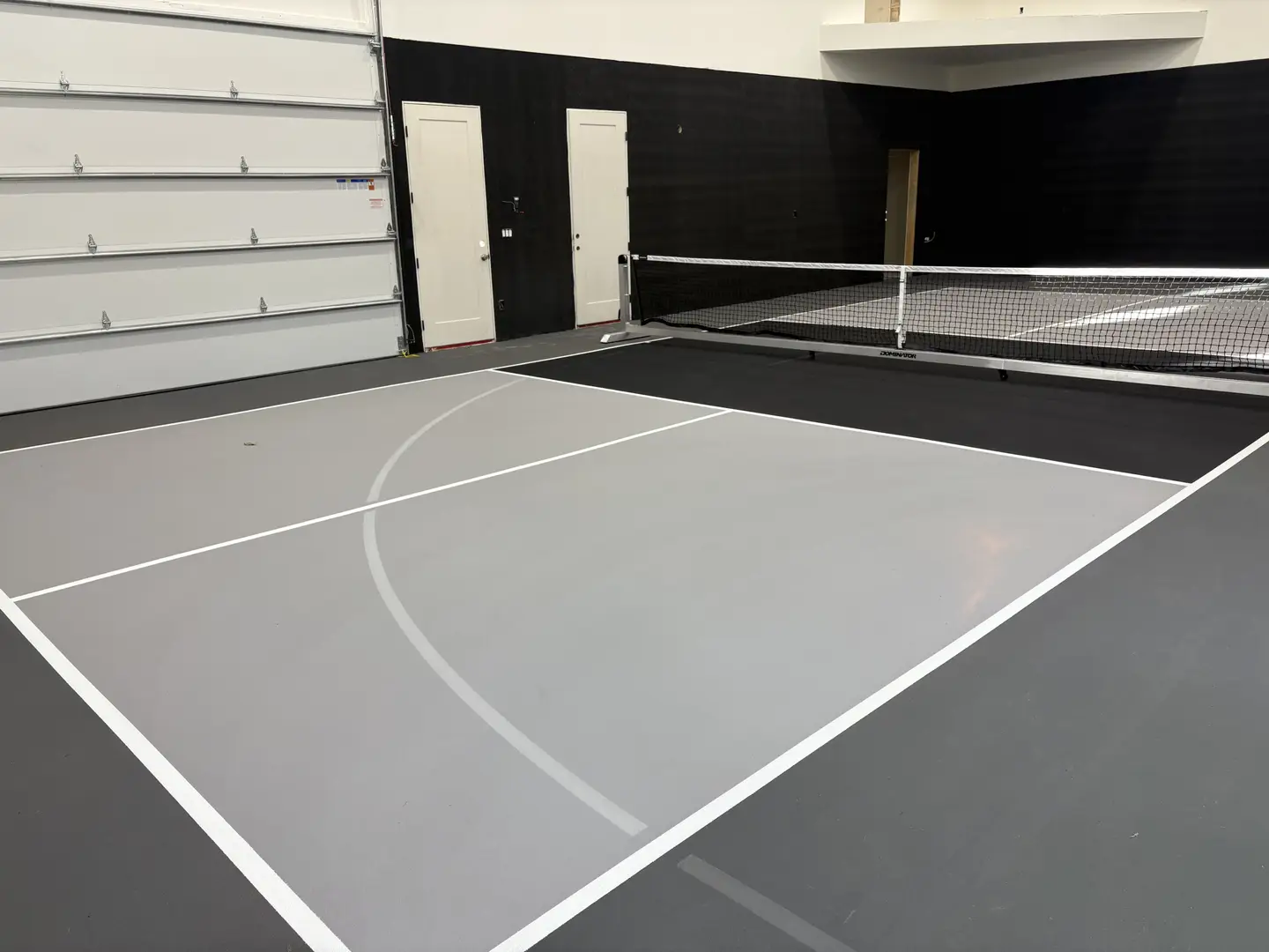 Indoor pickleball court with gray surface and white lines.