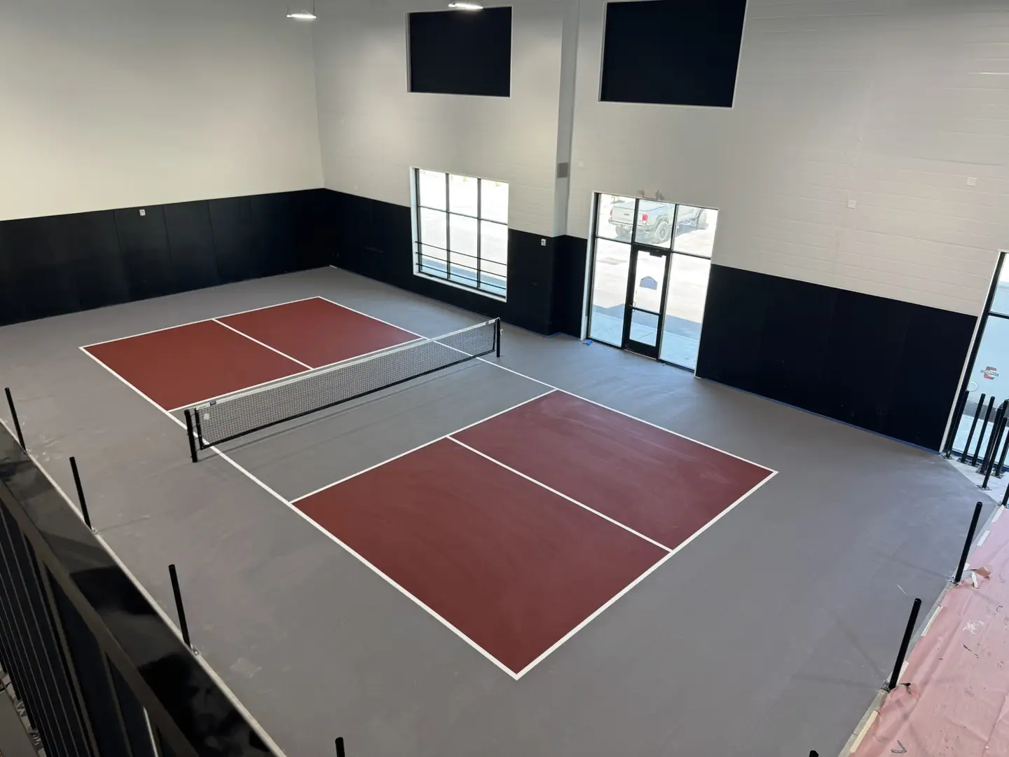 Indoor pickleball courts with maroon playing surfaces and a net.