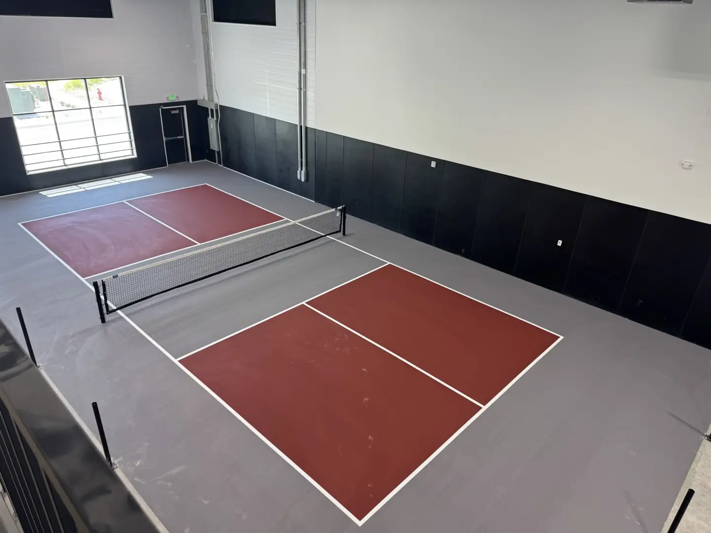 Indoor pickleball courts with maroon playing surfaces and grey surrounds.