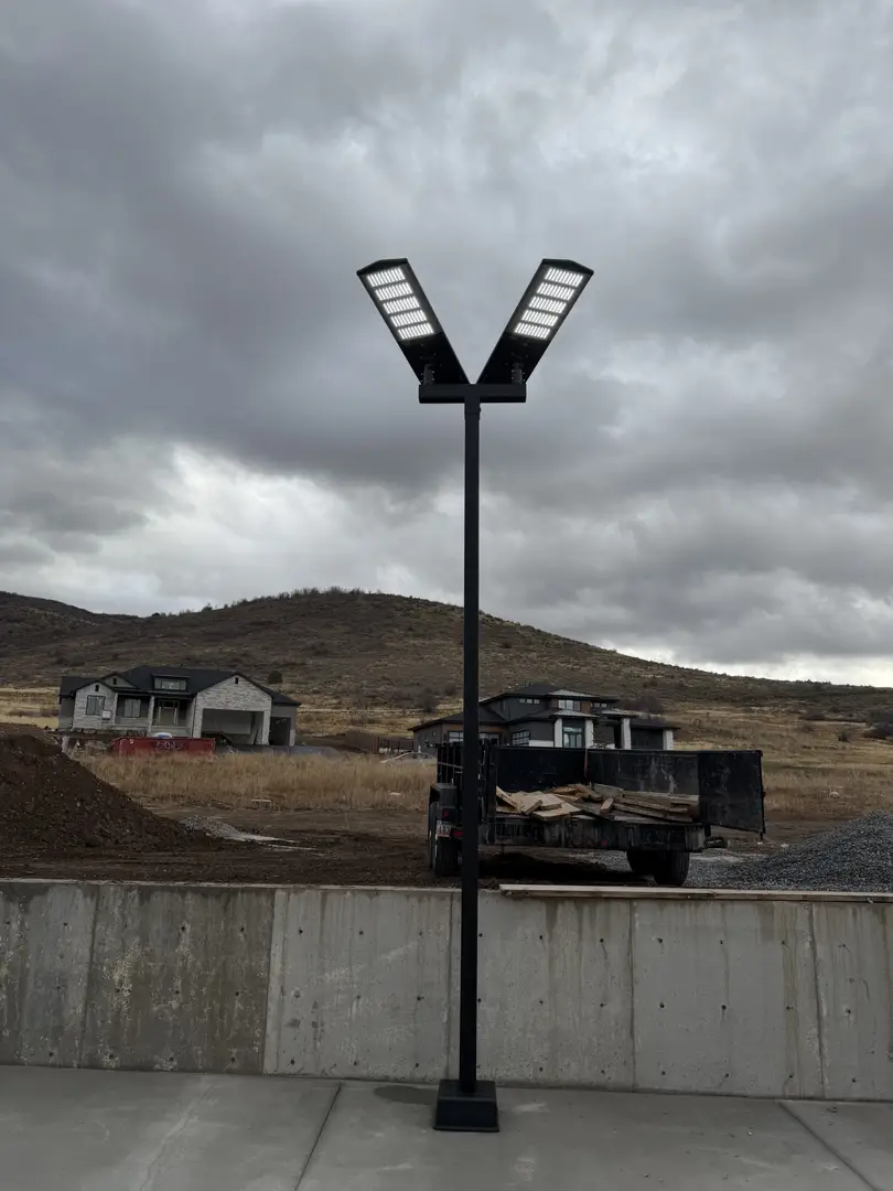 Modern V-shaped LED street light on a pole, with houses and hills in the background.