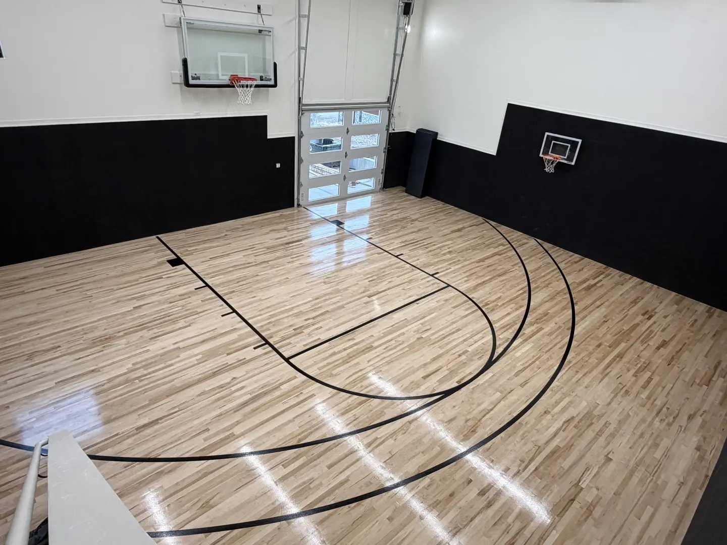 Indoor basketball court with polished wood floor and black walls.