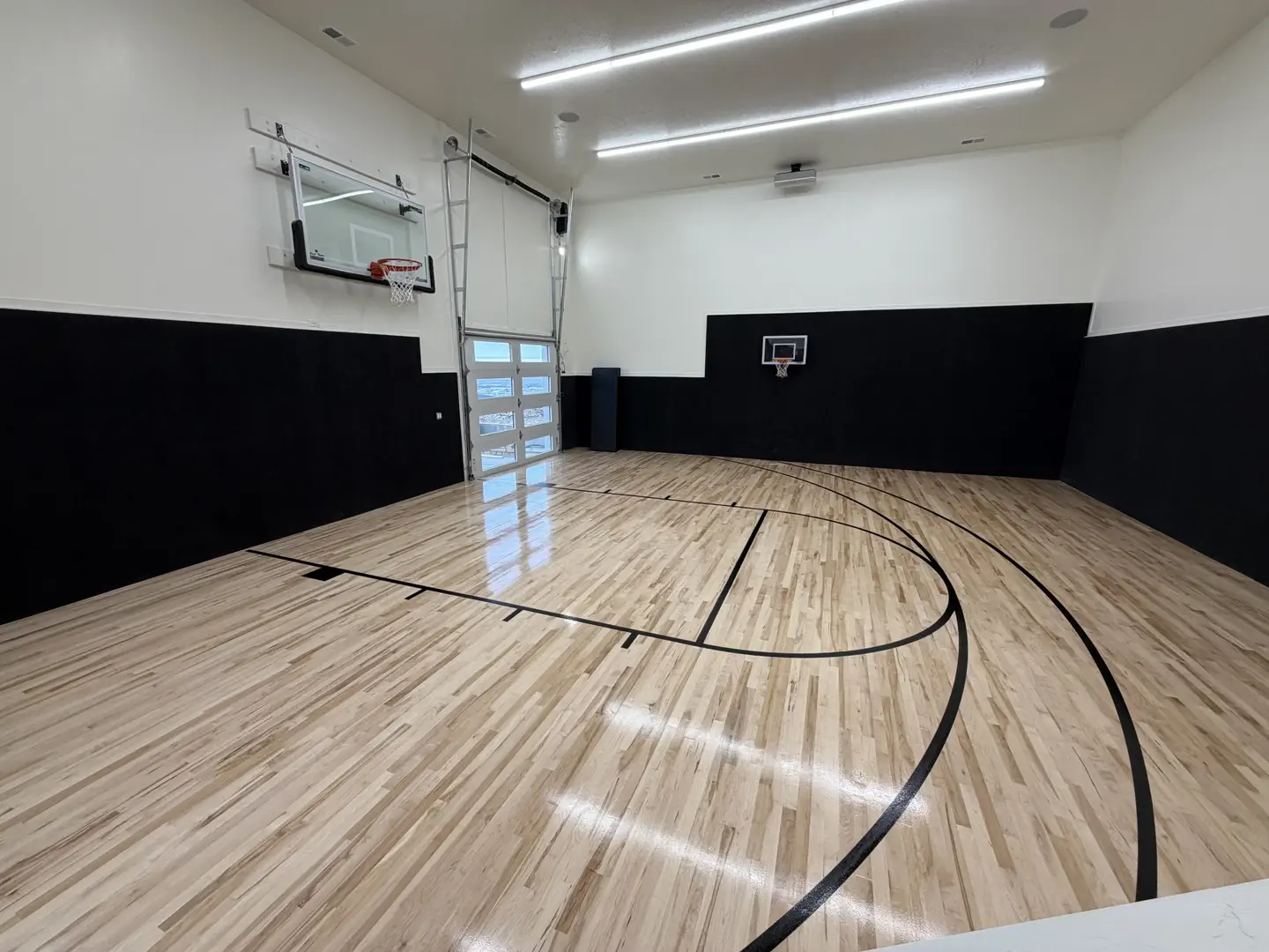 Indoor basketball court with polished wood floor and black walls.