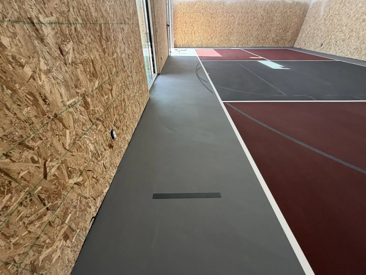 New indoor sports court with dark grey and maroon flooring.