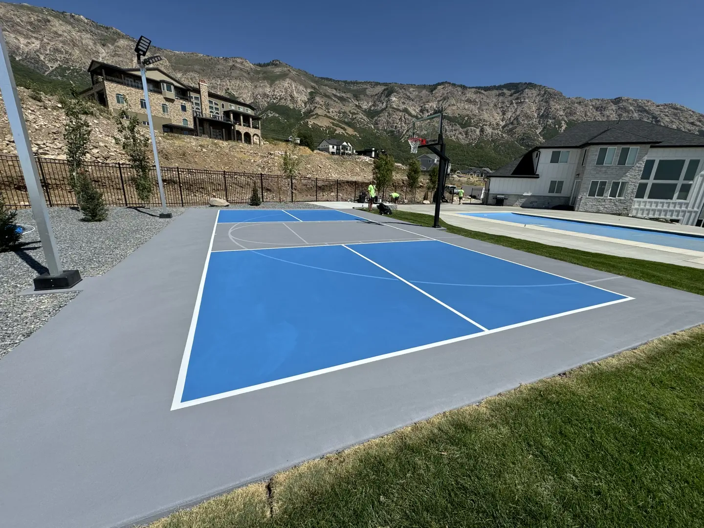 Newly painted blue and gray basketball court with a mountain backdrop.