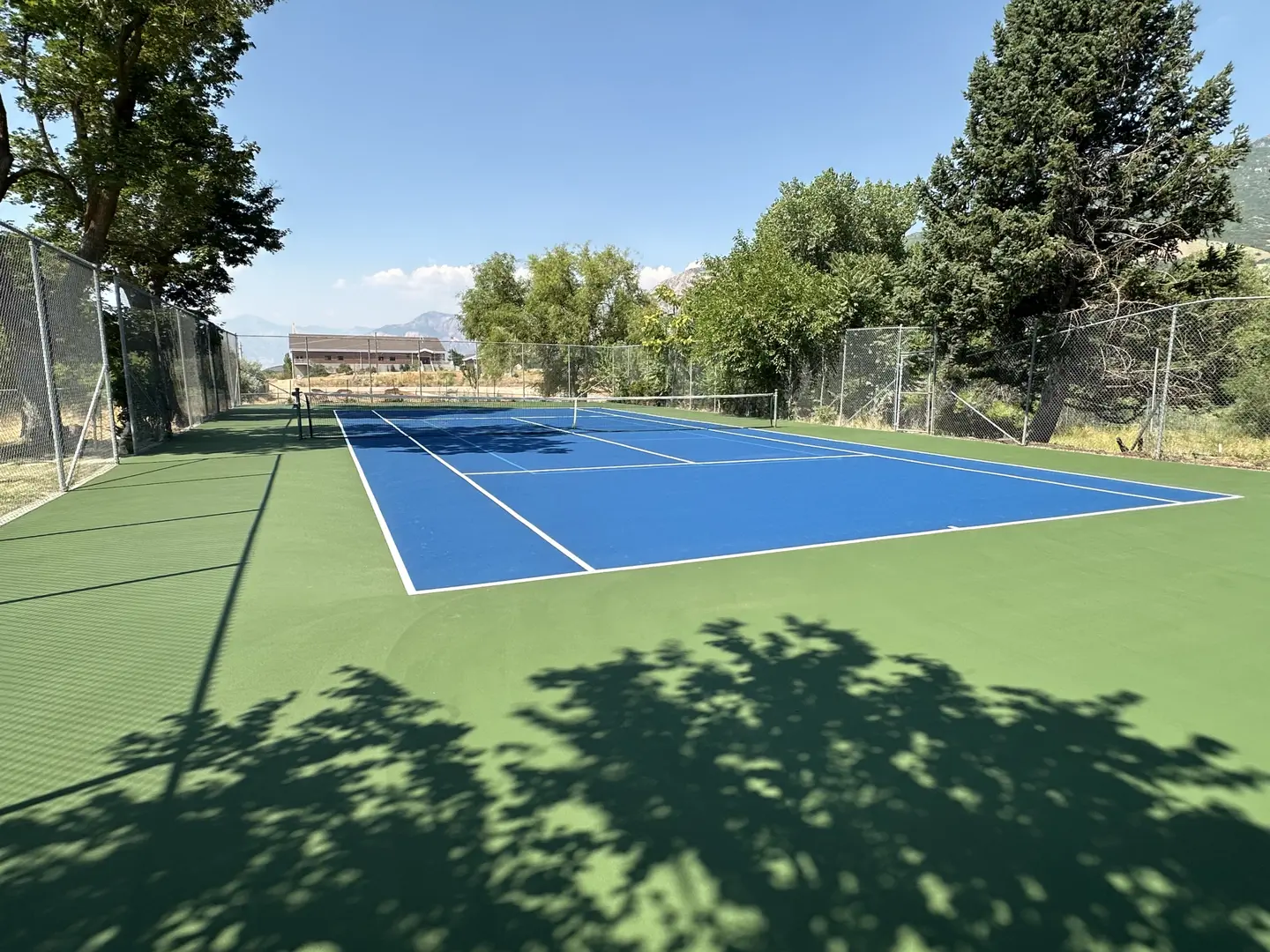 Bright blue tennis court with green surround and trees.