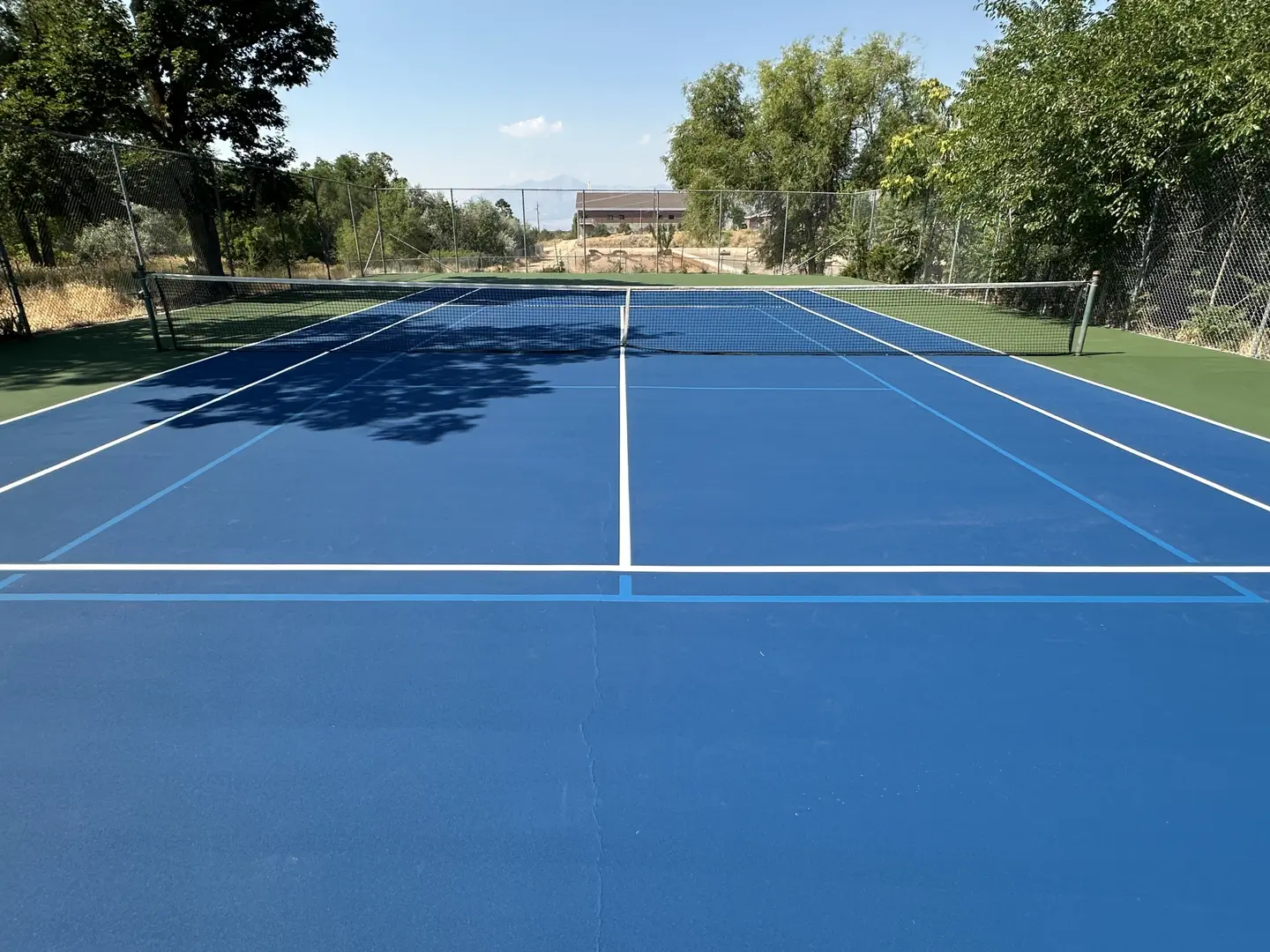 Blue tennis court with net and surrounding trees