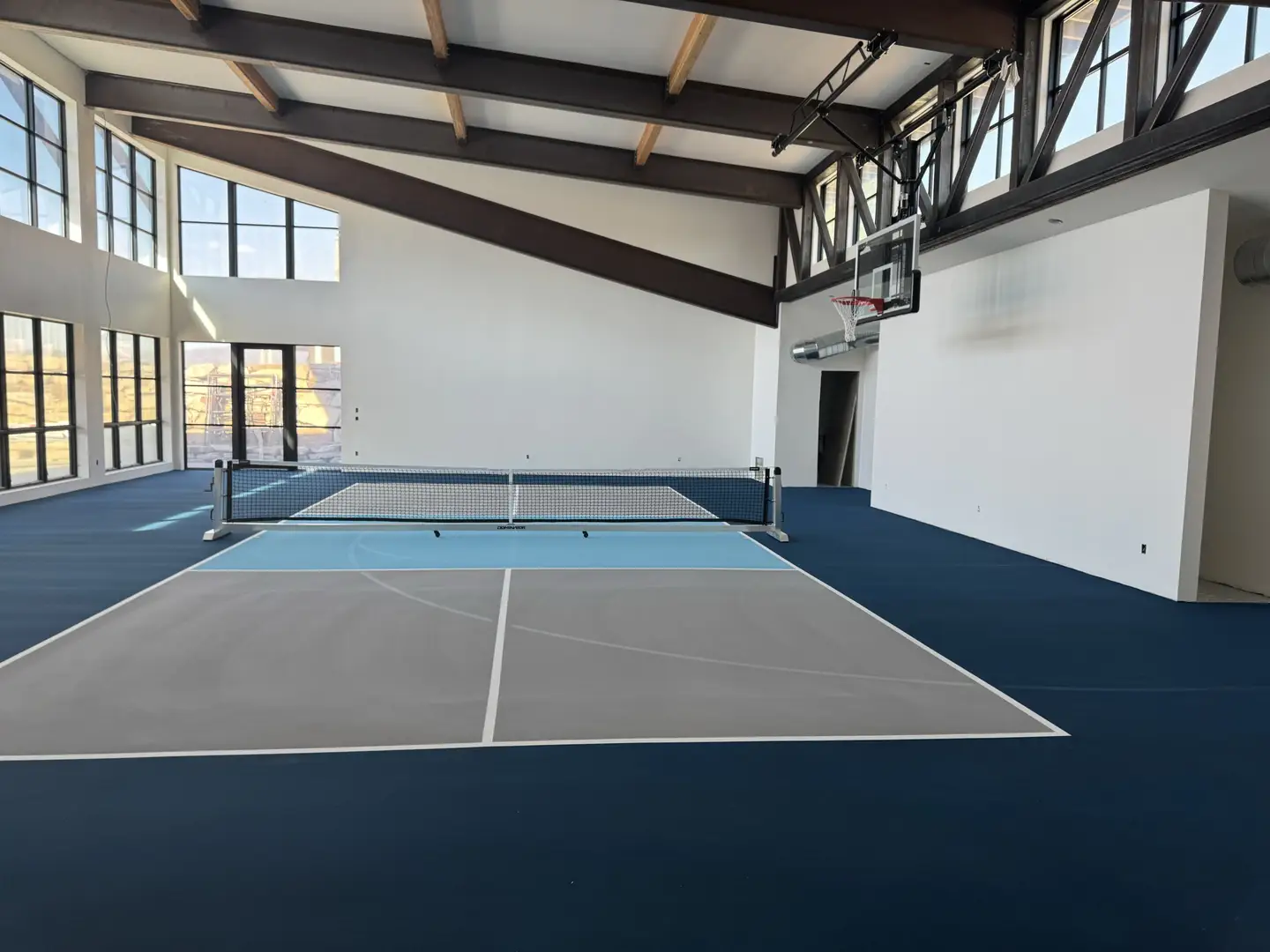 Indoor pickleball court with basketball hoop and large windows