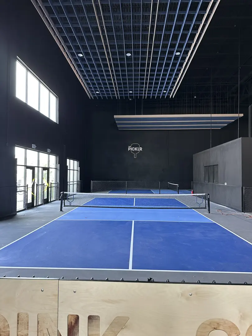 Indoor pickleball courts at The Picklr with blue surfaces and nets.