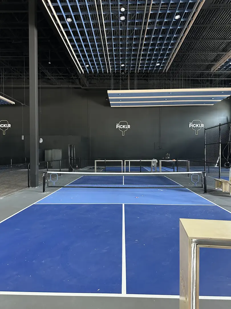 Indoor pickleball court with blue playing surface and modern lighting.