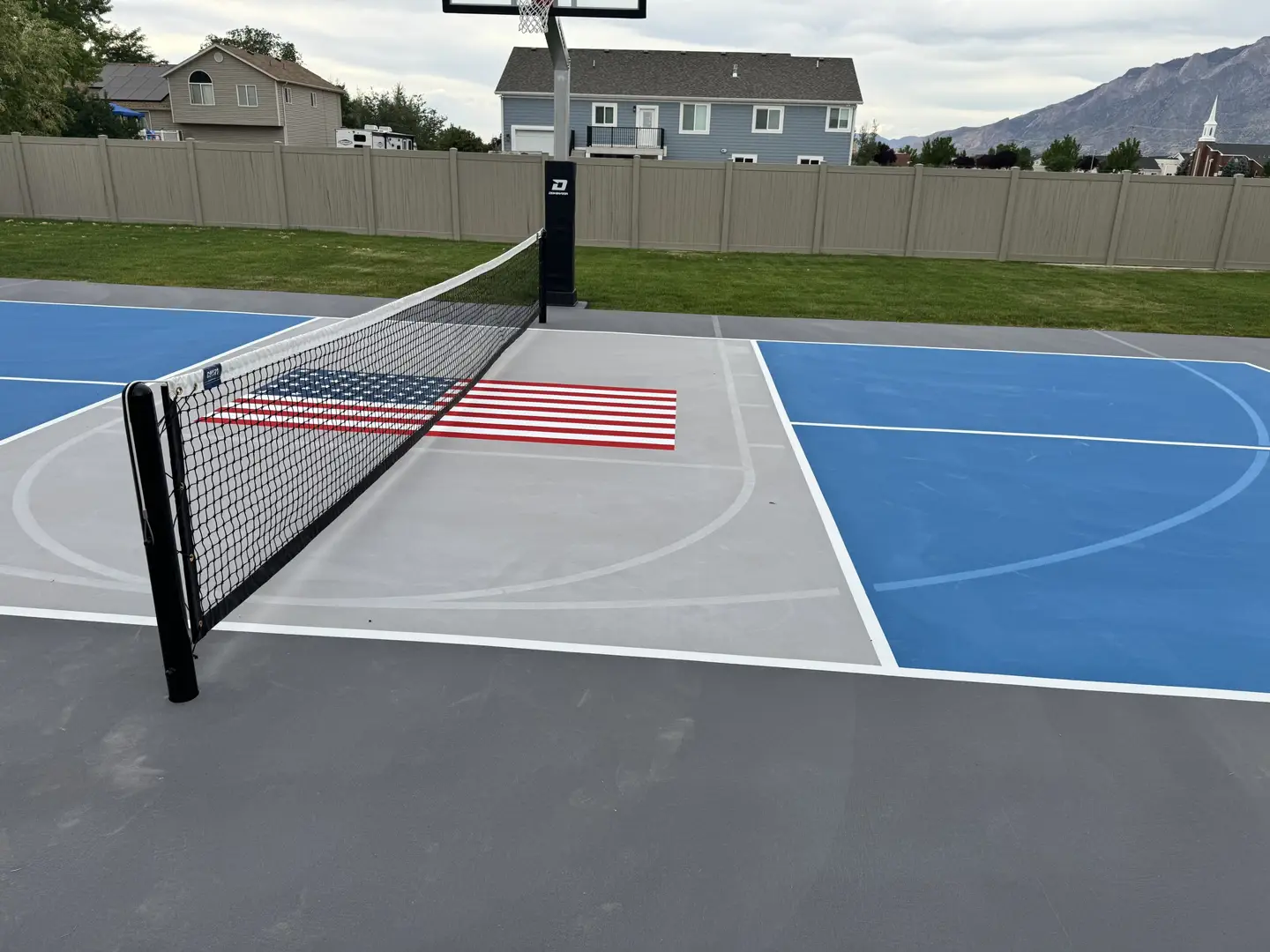 Multi-sport court with American flag design, basketball hoop, and net.