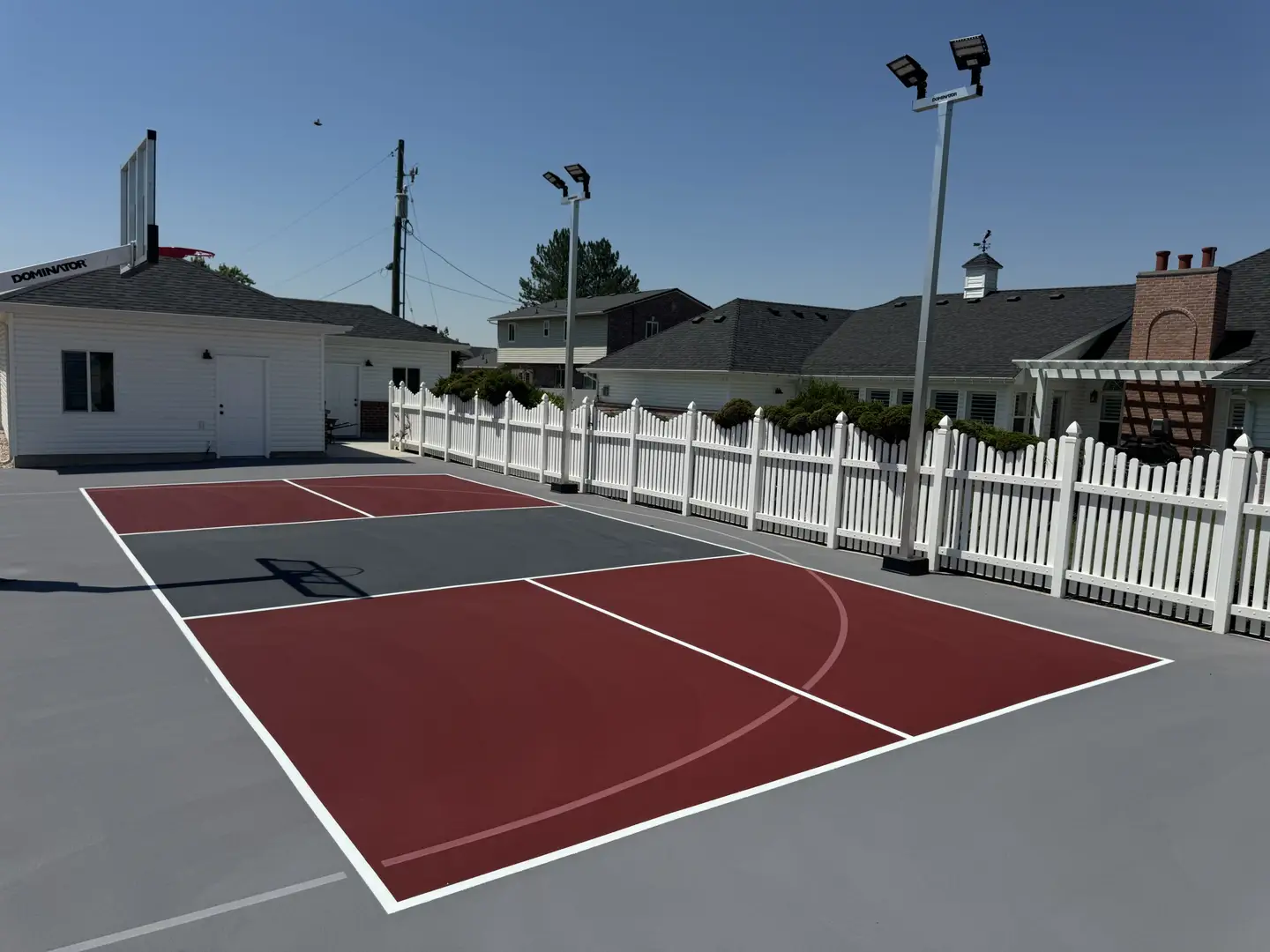 Modern backyard basketball court with red and gray surfacing and lighting.