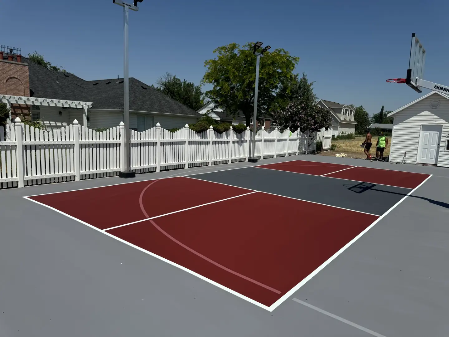 Newly painted basketball court with red and gray sections in a residential backyard.