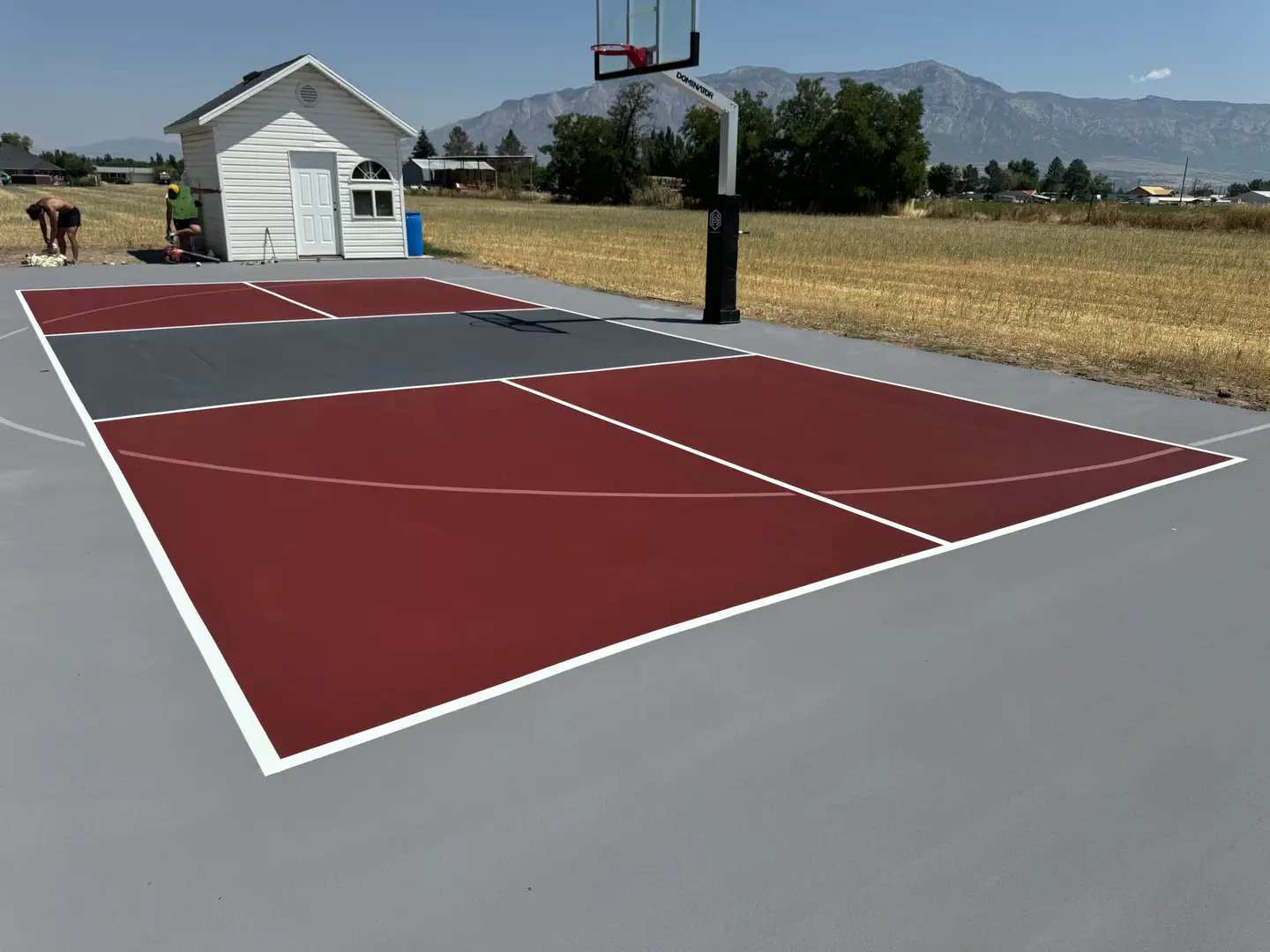 Newly painted basketball court with red and grey sections and white lines.