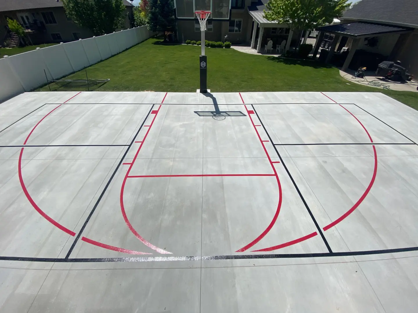 Newly painted backyard basketball court with red and black lines.