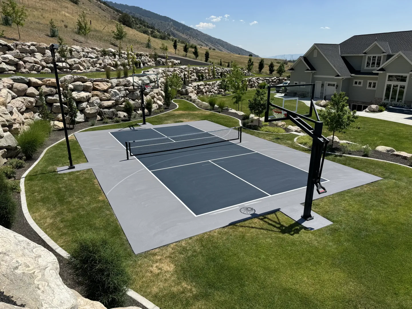 Multi-sport court with basketball hoop and net in a backyard.