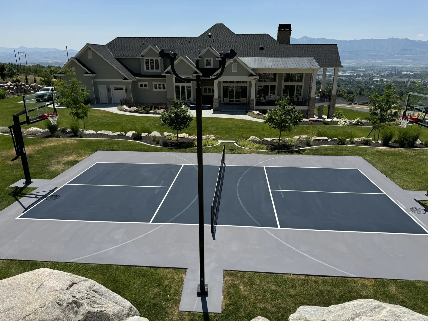 Multi-sport court with basketball hoops and volleyball net in a backyard.
