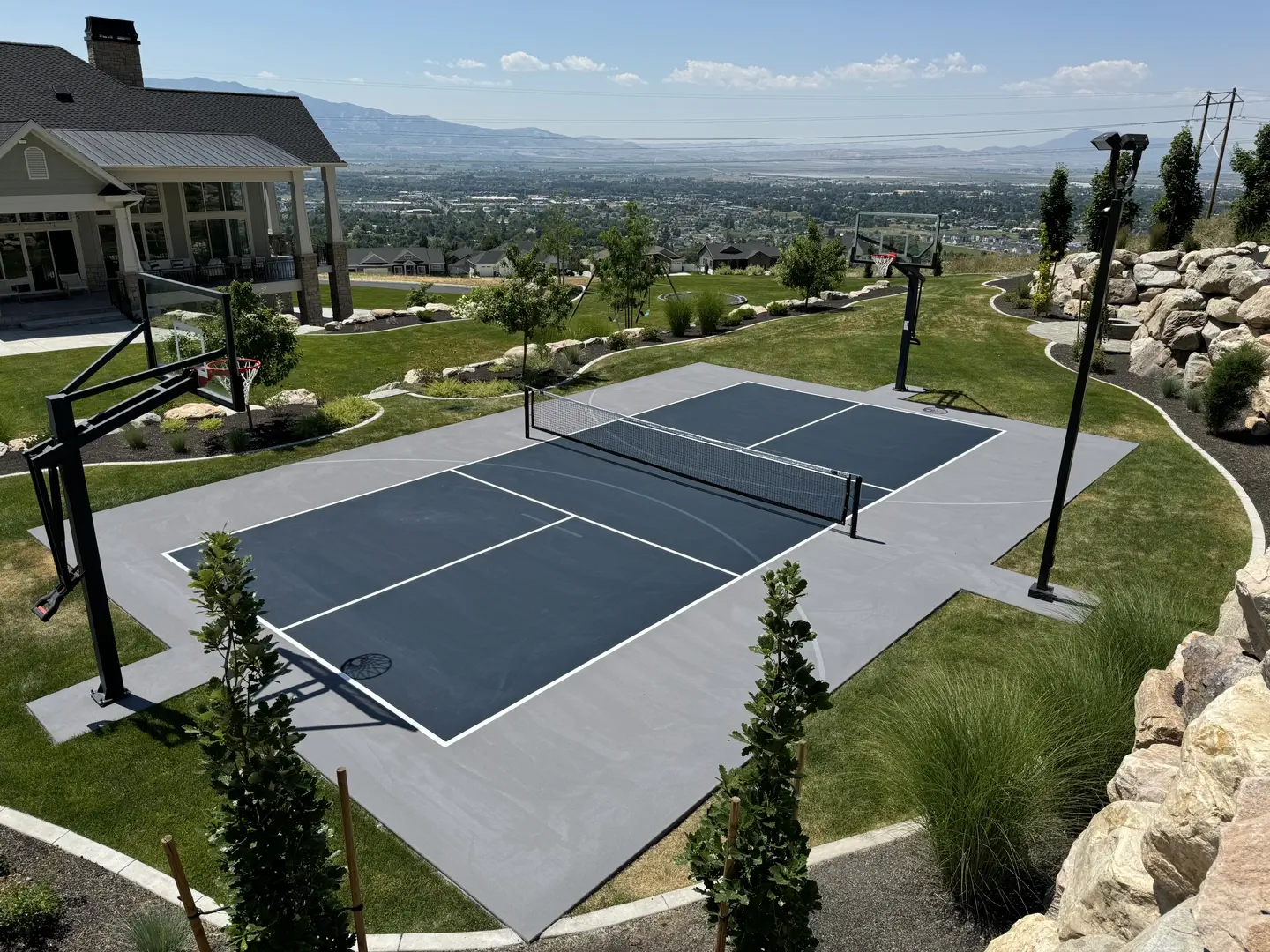 Modern multi-sport court with basketball hoop and pickleball net in a scenic backyard.