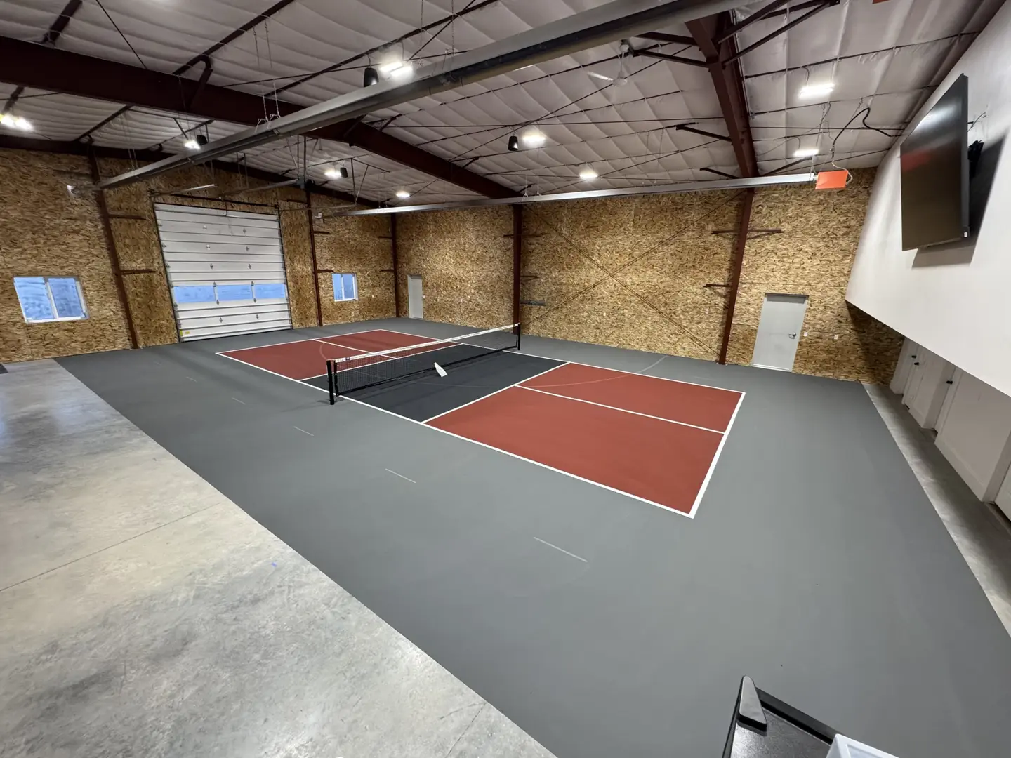 Indoor pickleball court with red and black playing surface.