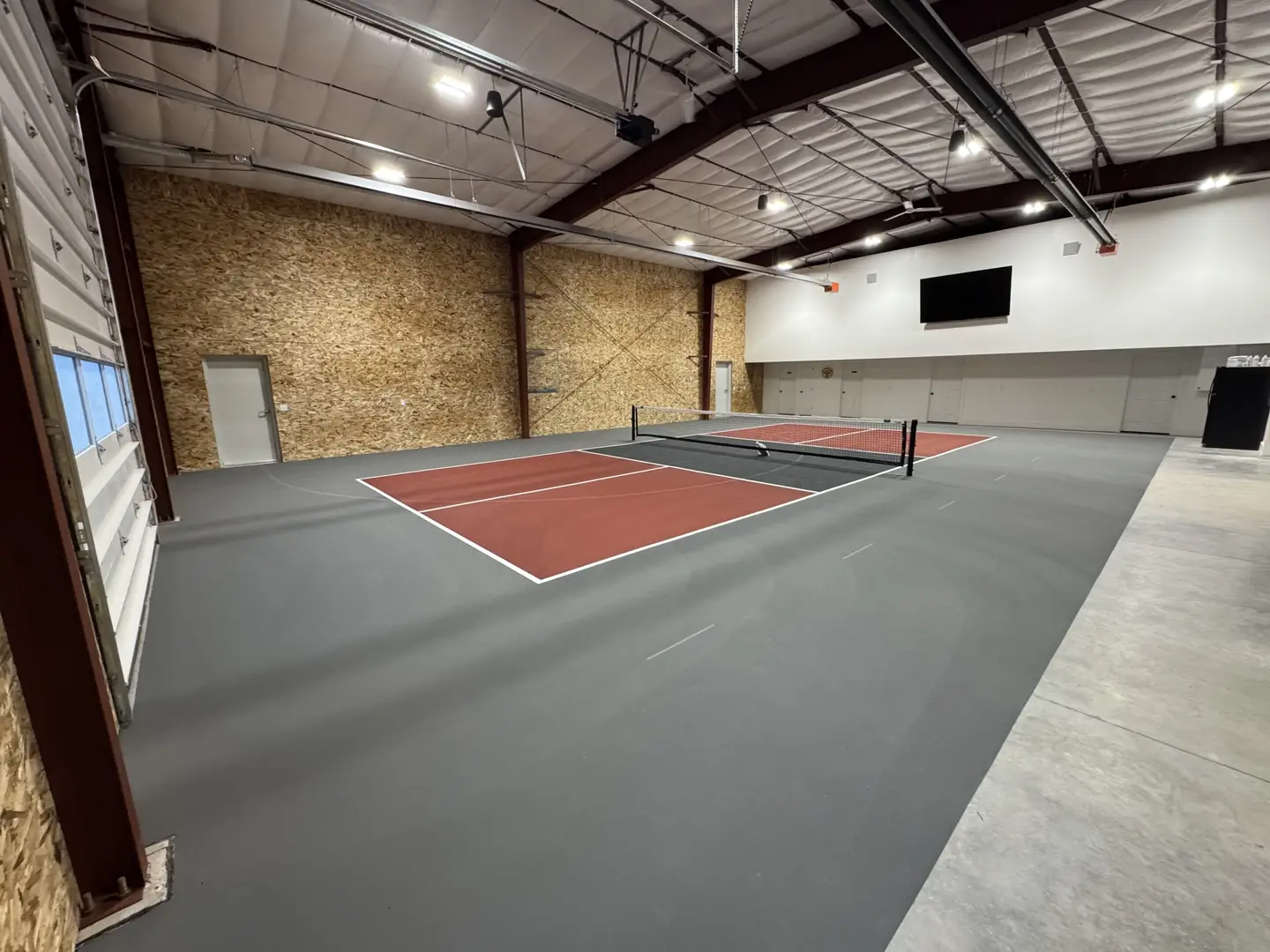 Indoor pickleball court with red and grey playing surfaces.