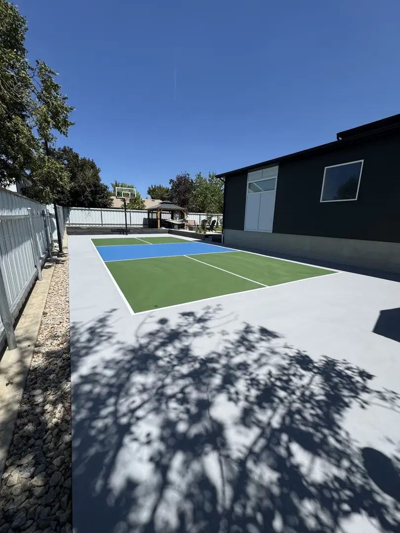 Backyard pickleball court with basketball hoop and gazebo.