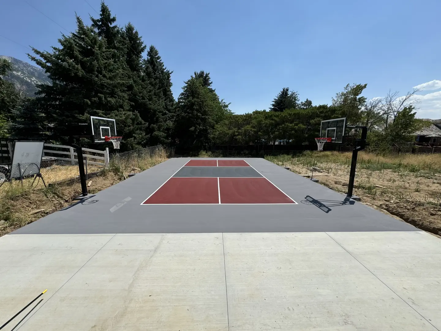 Newly painted basketball court with red and grey sections and two hoops.