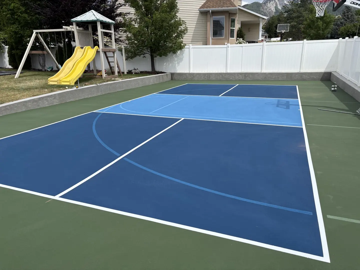 Blue and green multi-sport court with basketball hoop and playground