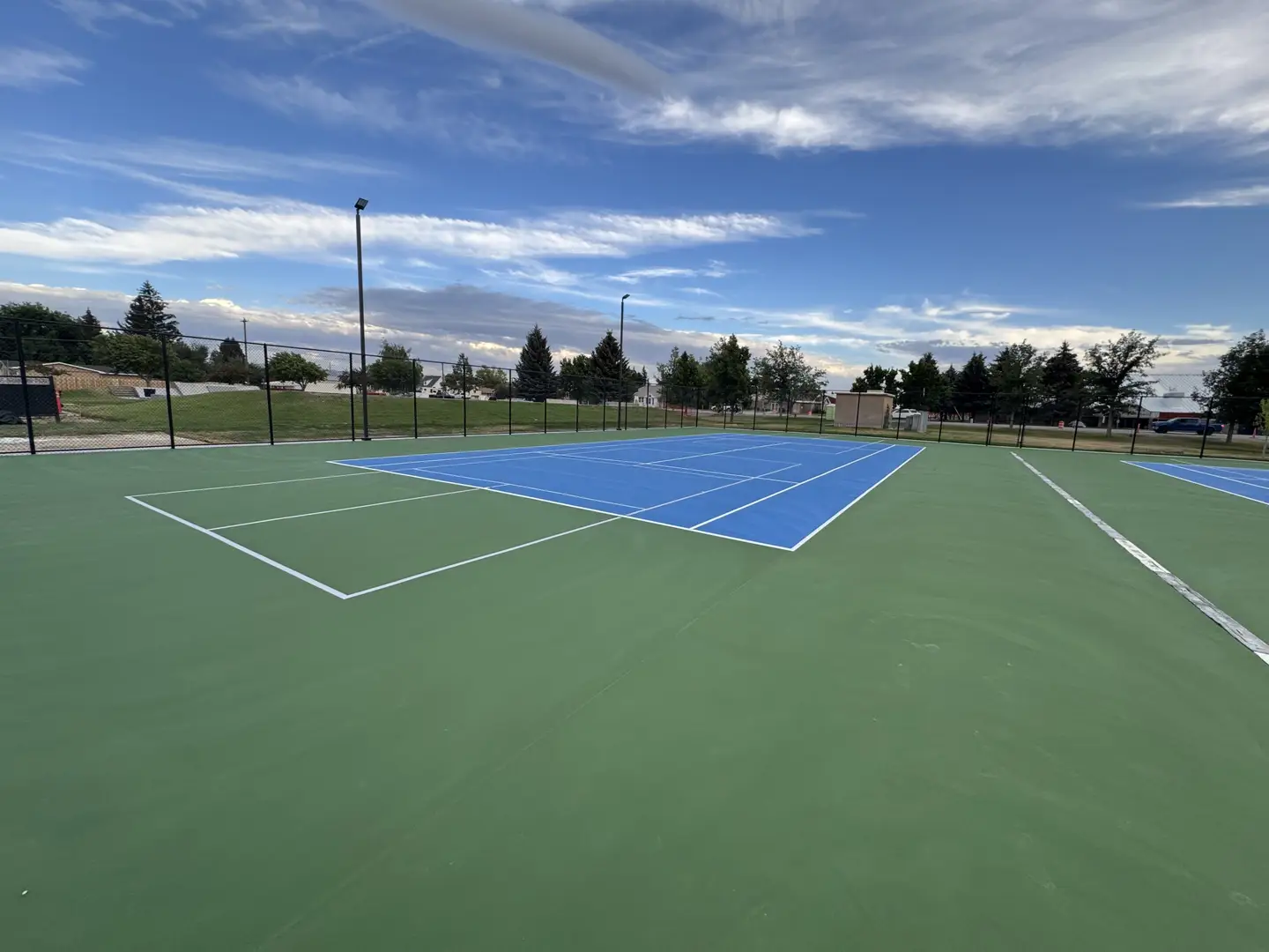 Newly resurfaced blue and green tennis courts with white lines and a cloudy sky.