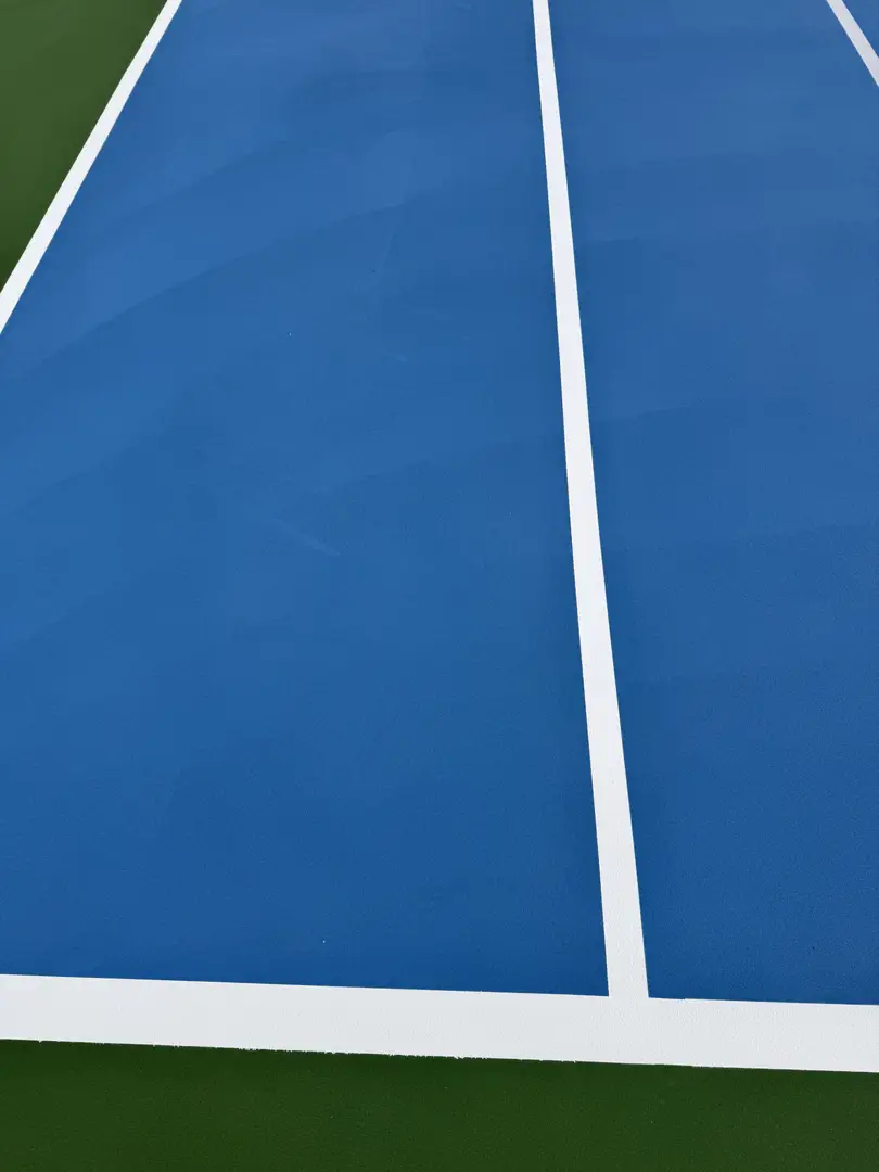 Vibrant blue tennis court with white lines and green outer edges