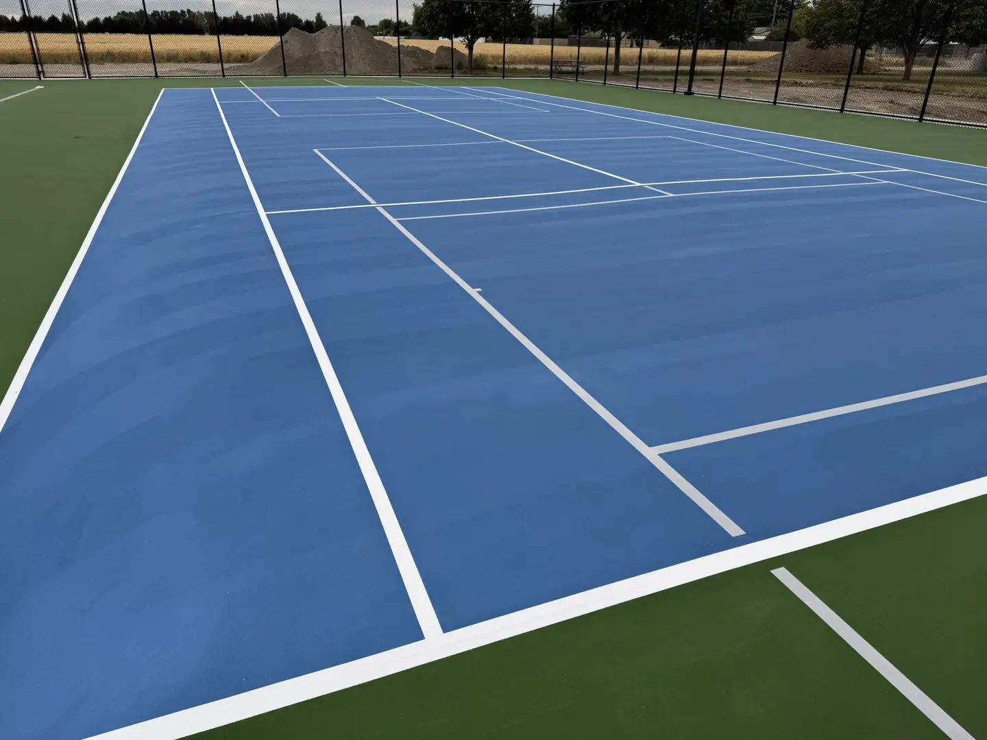 Newly painted blue tennis court with green out-of-bounds area.