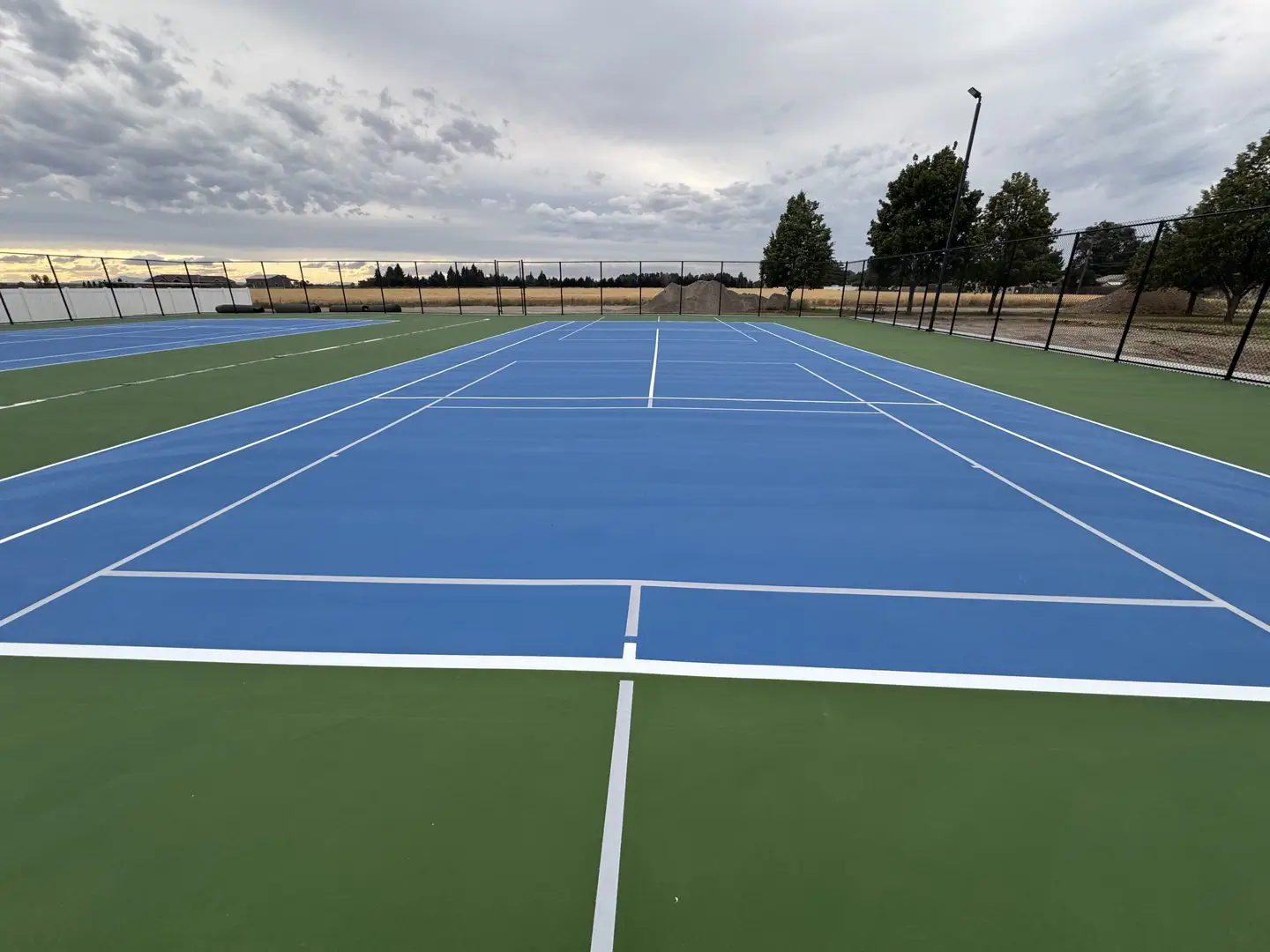 Vibrant blue tennis court with green surrounds and white lines, ready for play.