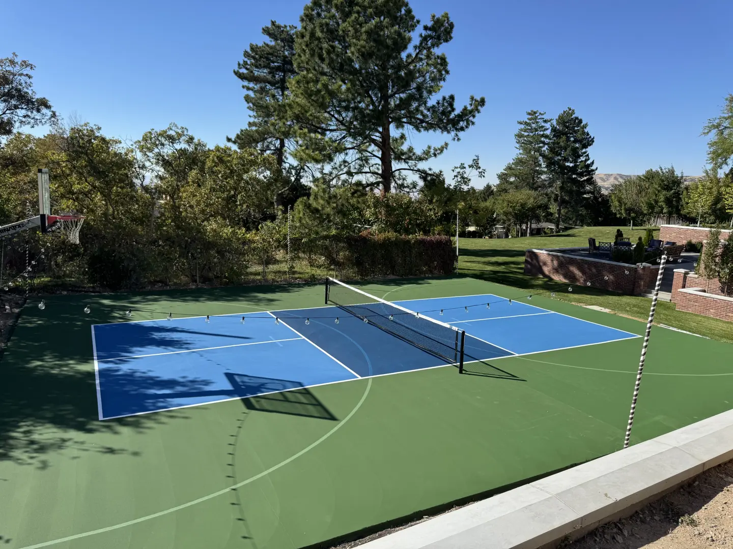 Outdoor pickleball court with basketball hoop and blue playing surface.