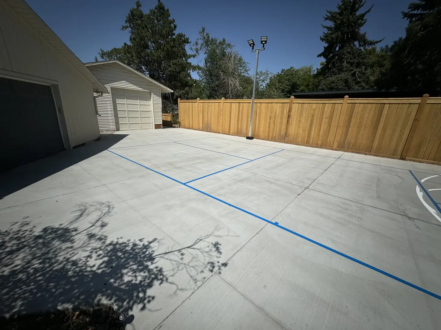 Newly poured concrete basketball court with blue lines and a wooden fence.