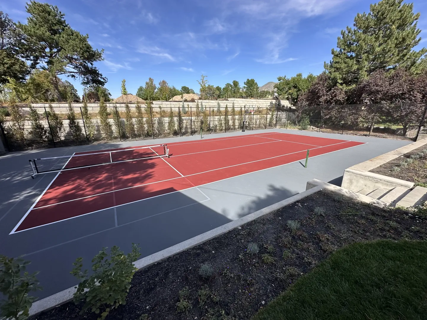 Red and gray tennis court with net and blue sky.