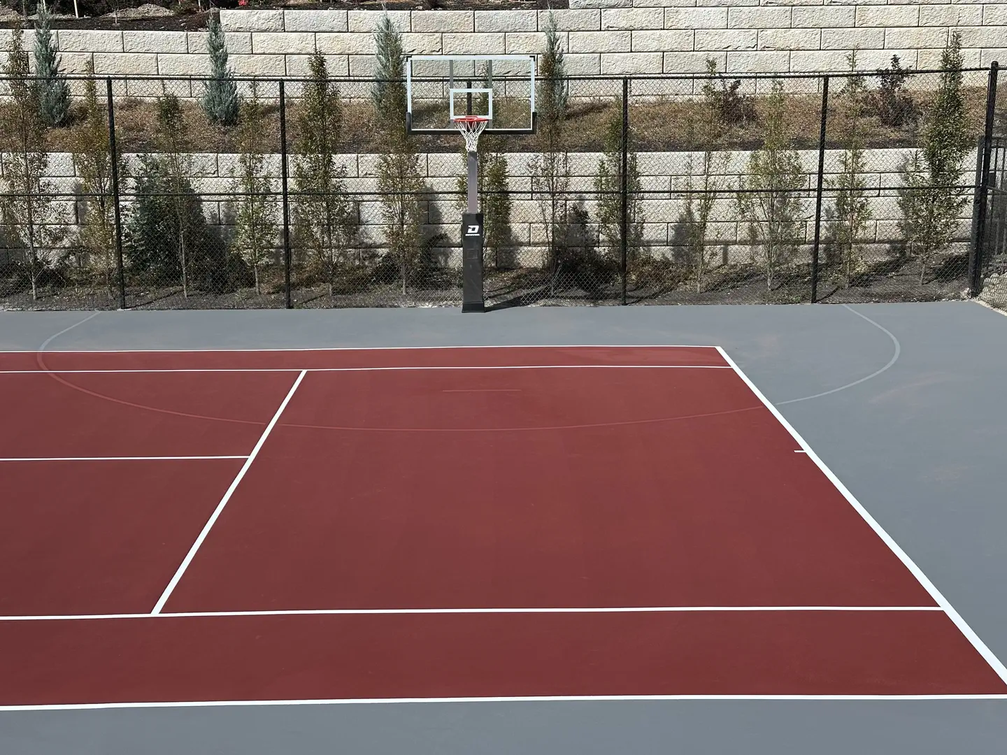Red and grey basketball court with hoop and fence