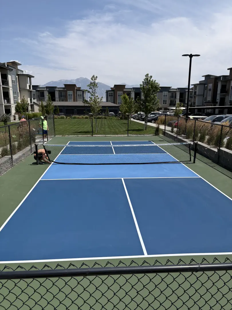 People playing pickleball on a bright blue court with mountains in the background.