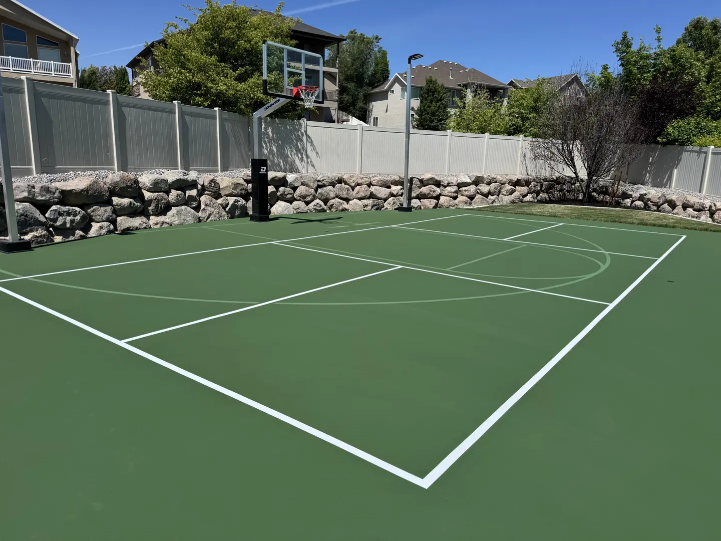 Green backyard basketball court with white lines and a basketball hoop.