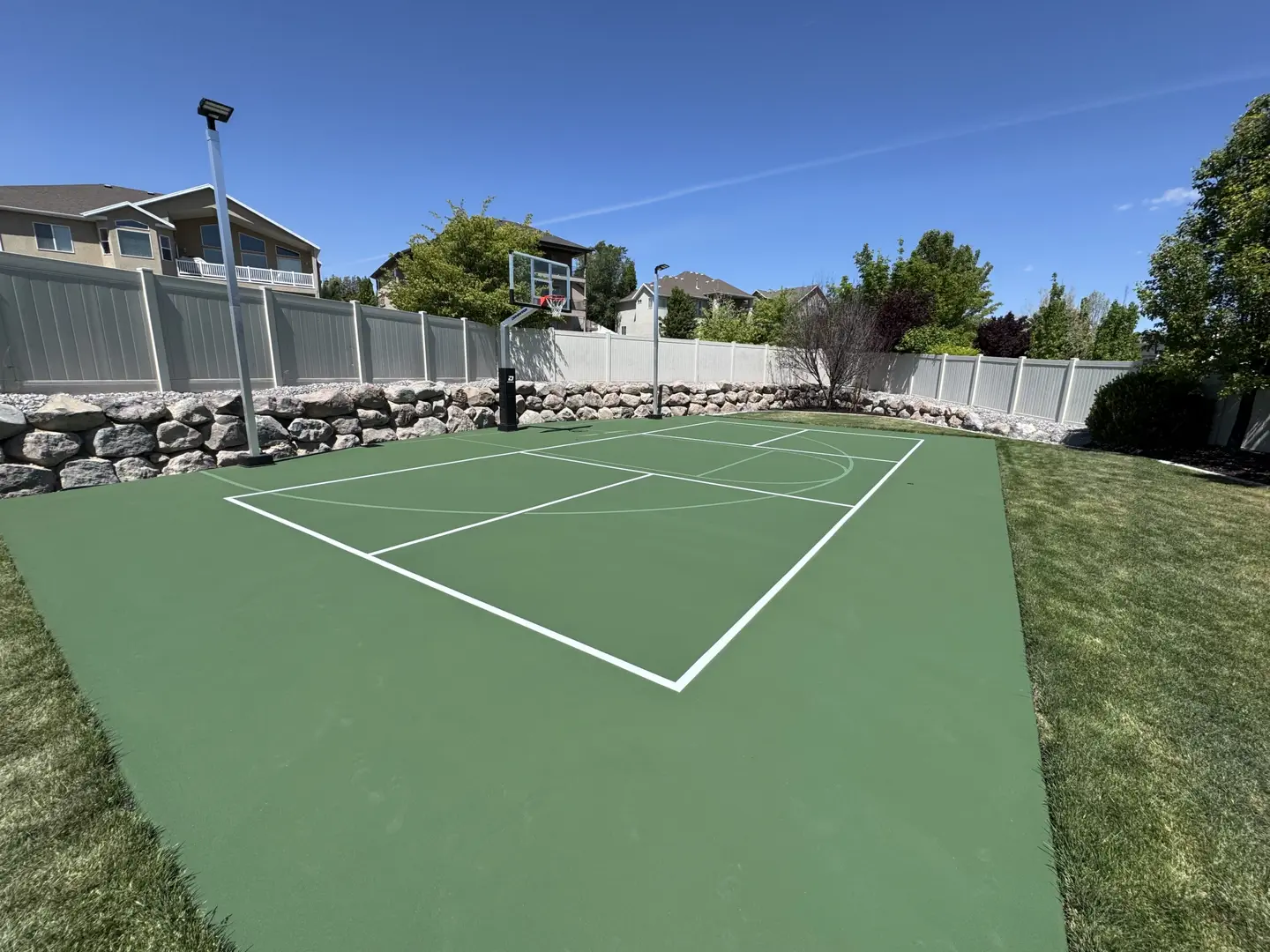 Green backyard basketball court with white lines and a hoop.