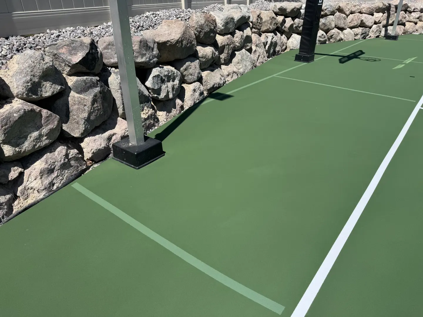 Green tennis court with white lines and a rock wall backdrop.
