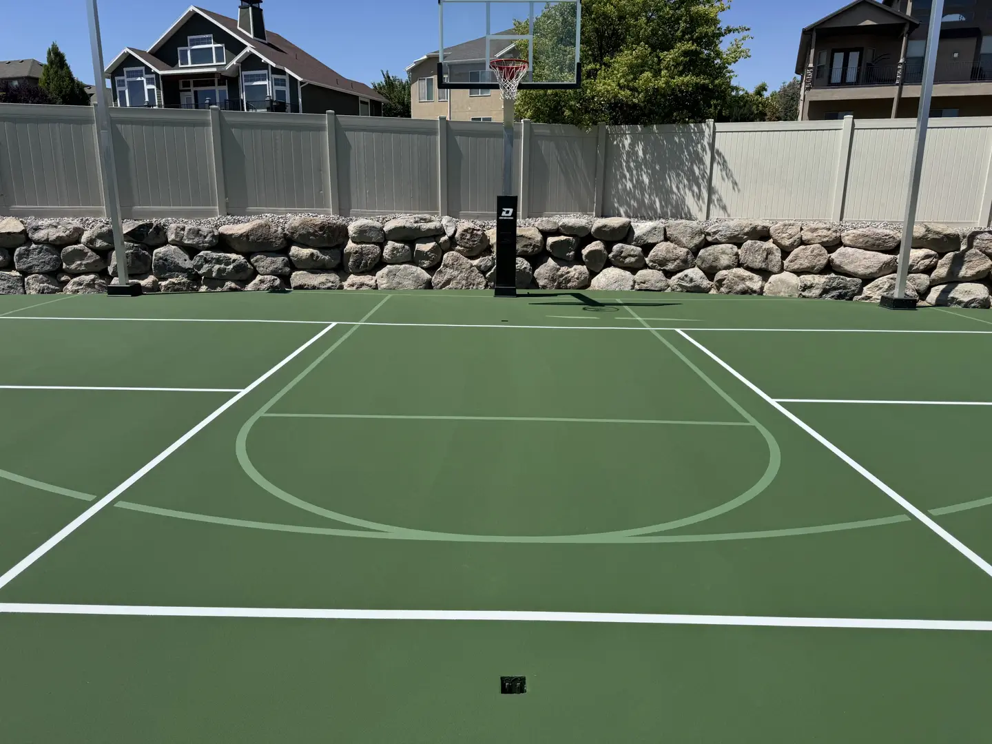 Green basketball court with white lines and a basketball hoop.