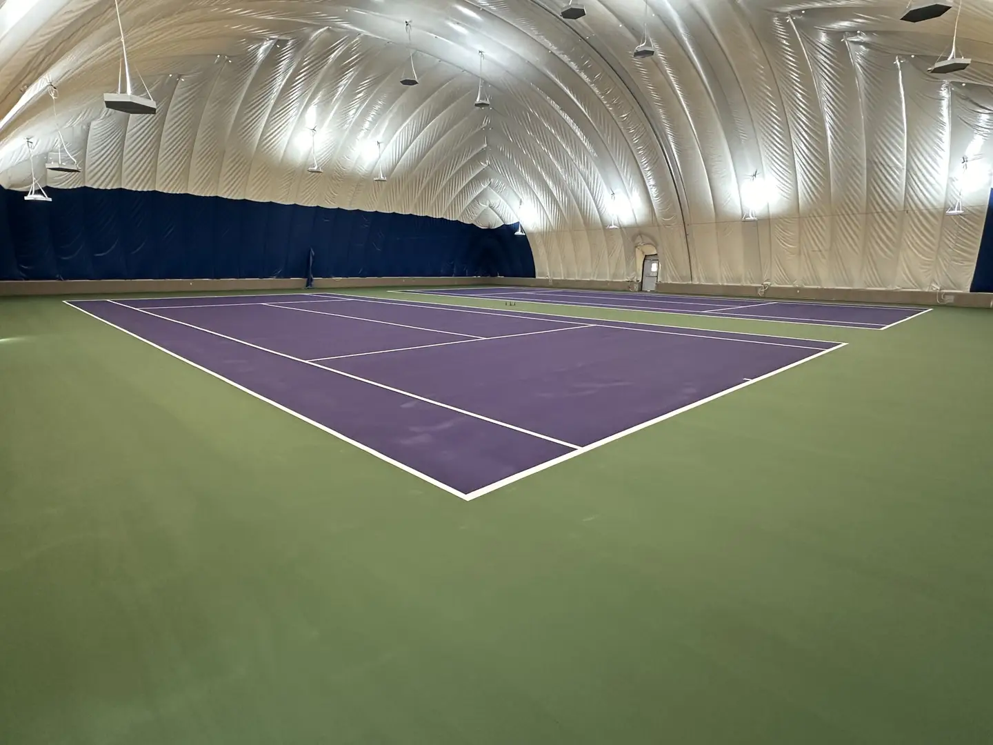 Indoor tennis courts with purple playing surface and green surrounds under an inflatable dome.