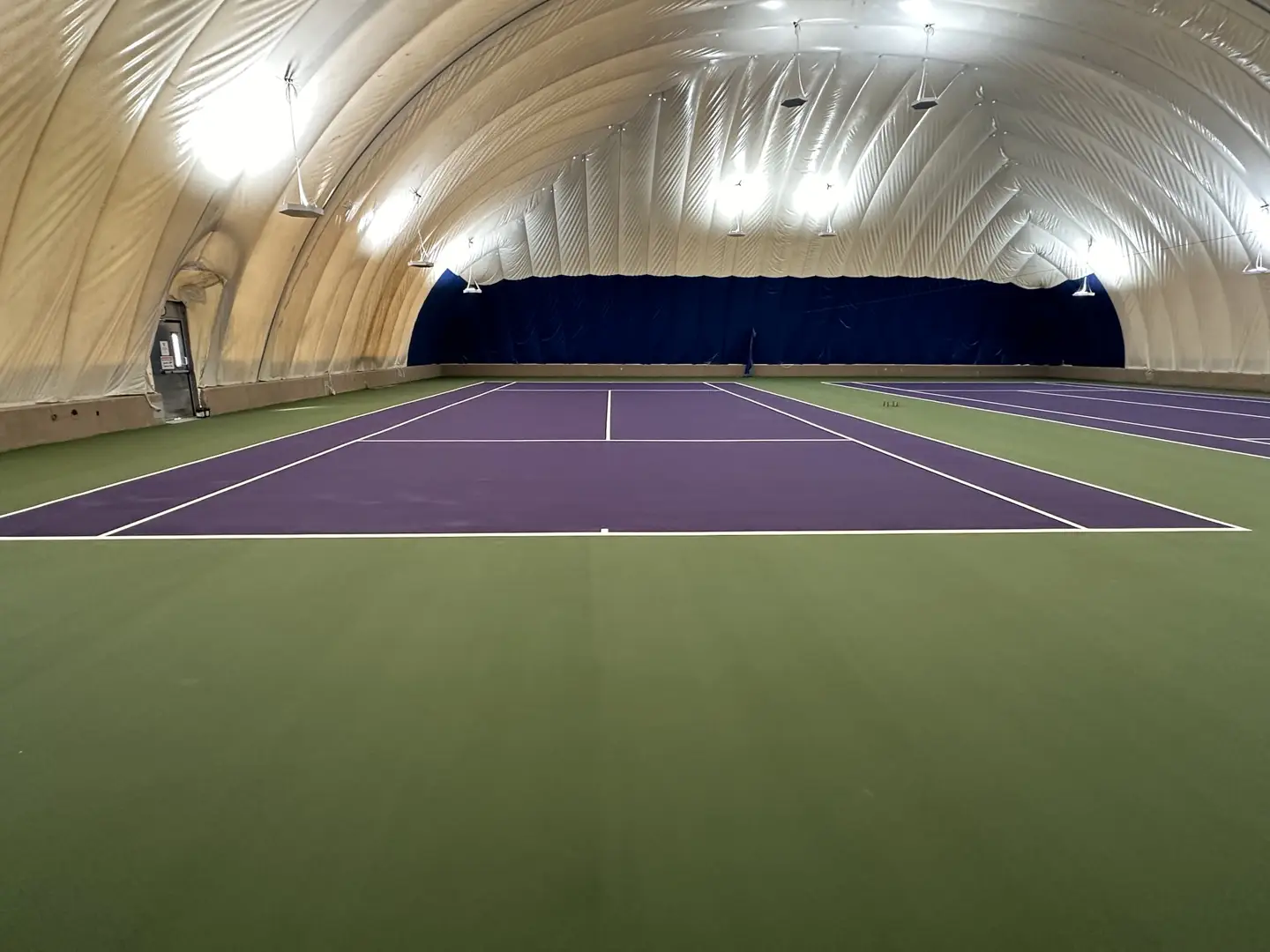 Indoor tennis court with purple playing surface and green out-of-bounds area.