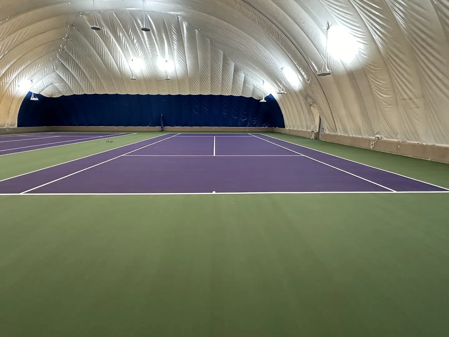 Indoor tennis court with purple and green courts under a white dome.
