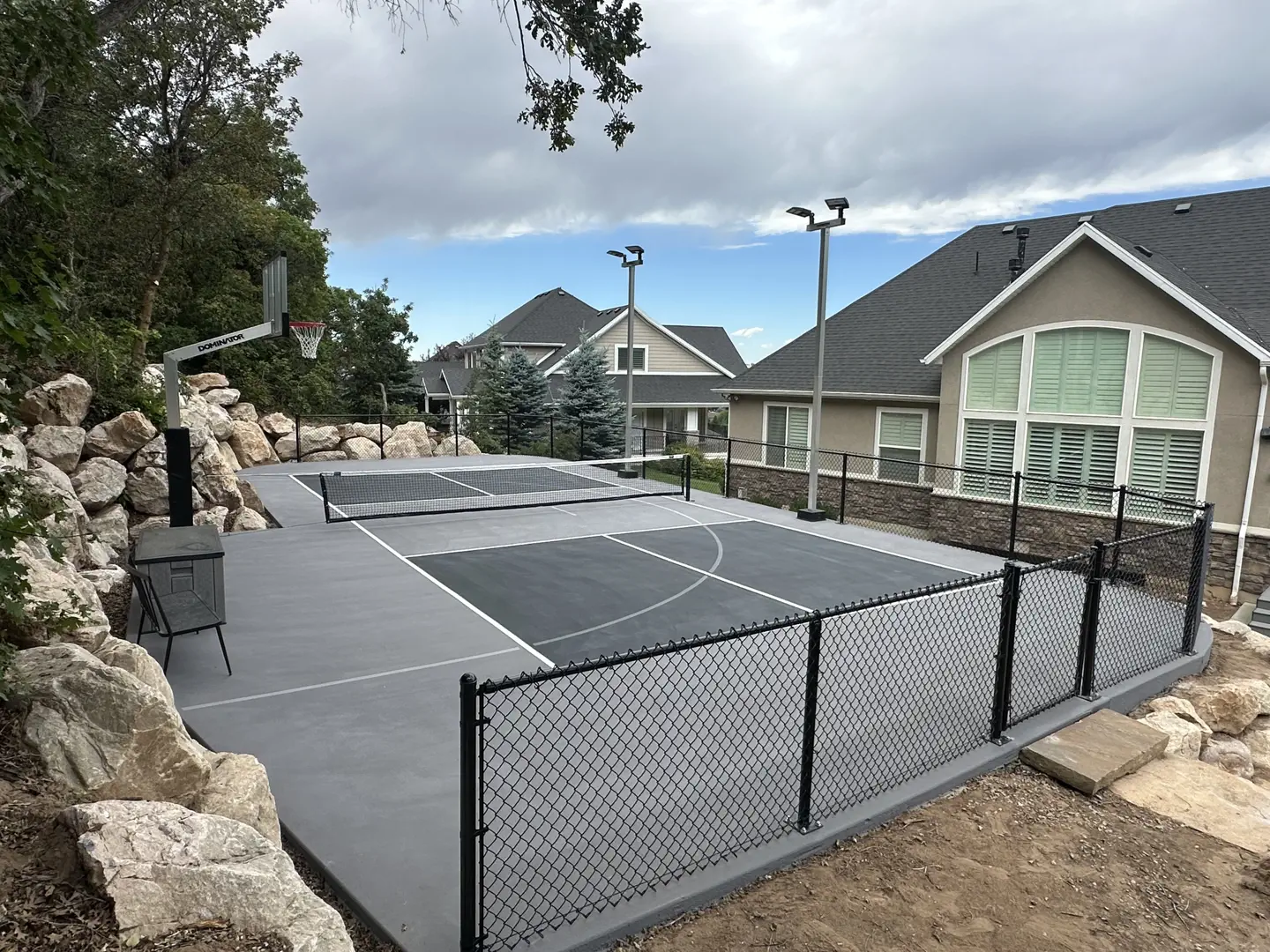 Backyard basketball and pickleball court with fencing and landscaping.