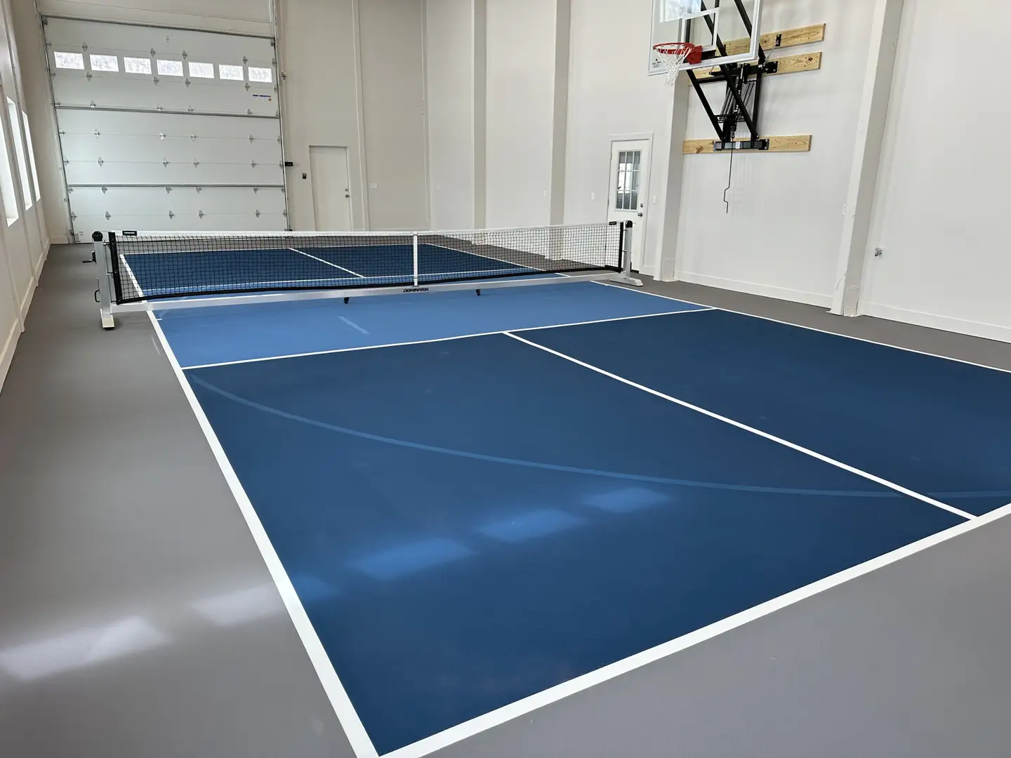Indoor pickleball court with blue surface and basketball hoop